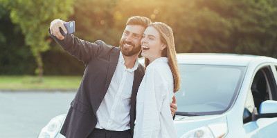 young couple hugging and smiling while taking selfie in front of car