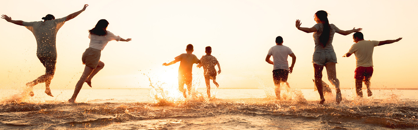 group of people running and splashing in the surf with sun setting on horizon